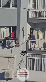 İzmir'de bir klima tamircisi, binanın dış cephesindeki klima ünitesinin üzerine yatarak çalıştı.